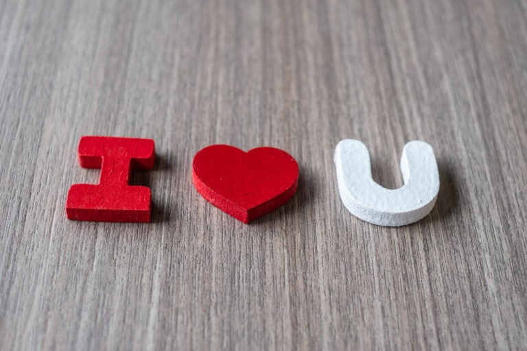Red heart between "I" and "U" symbols on wooden surface.