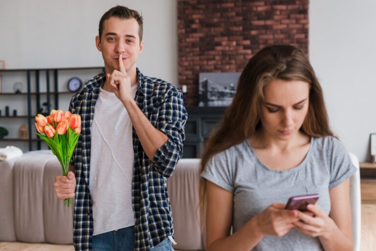 A man holding flowers making a "shh" gesture behind a woman looking at her phone, representing the dilemma of disclosing herpes in a dating relationship.