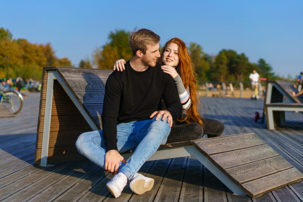 A supportive and connected young couple sitting together on an outdoor wooden bench, illustrating positive outcomes and connections for people exploring Herpes Dating in Michigan.